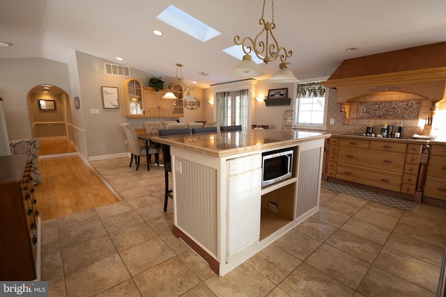 kitchen with lofted ceiling, light tile patterned floors, a breakfast bar area, custom range hood, and a kitchen island