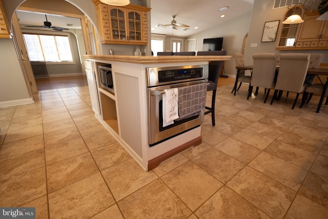 kitchen with ceiling fan, stainless steel appliances, a kitchen breakfast bar, light tile patterned flooring, and vaulted ceiling