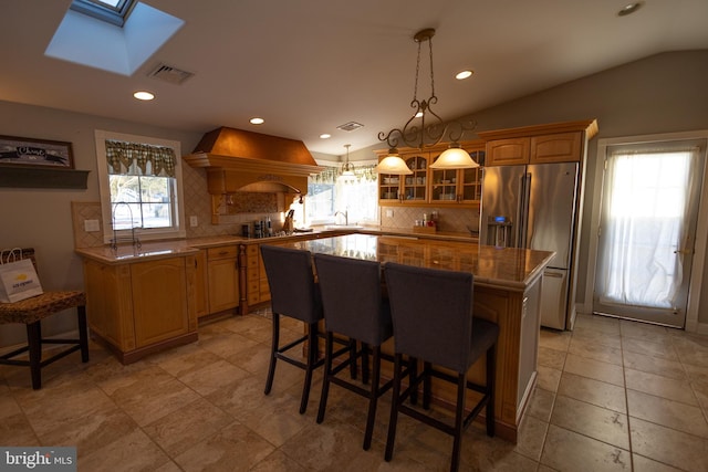 kitchen featuring lofted ceiling with skylight, high quality fridge, sink, custom exhaust hood, and a center island