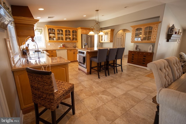 kitchen with lofted ceiling, appliances with stainless steel finishes, a kitchen island, pendant lighting, and backsplash