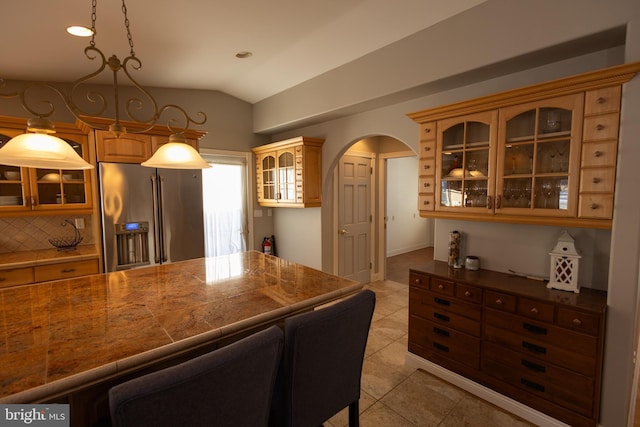 kitchen with light tile patterned flooring, lofted ceiling, stainless steel fridge, and decorative light fixtures