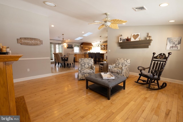 living room featuring ceiling fan, vaulted ceiling with skylight, and light hardwood / wood-style flooring