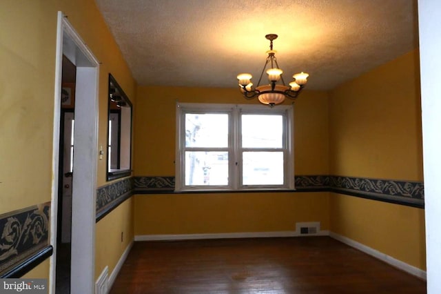 unfurnished room with dark hardwood / wood-style flooring, a textured ceiling, and a notable chandelier