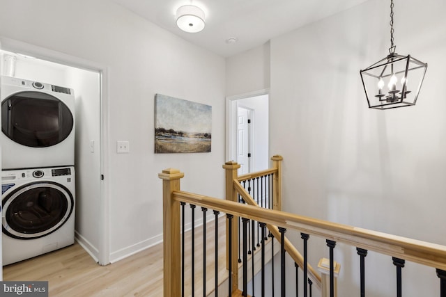 laundry room with an inviting chandelier, stacked washer / drying machine, and light hardwood / wood-style floors