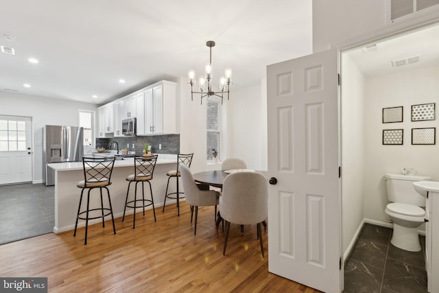 kitchen featuring backsplash, stainless steel appliances, white cabinets, a kitchen bar, and kitchen peninsula