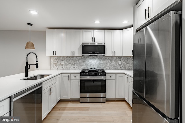 kitchen featuring pendant lighting, sink, white cabinets, stainless steel appliances, and light wood-type flooring