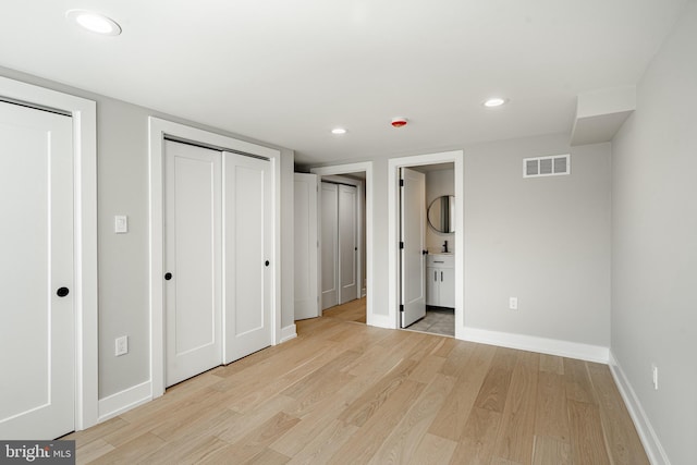 unfurnished bedroom with two closets, ensuite bath, and light hardwood / wood-style floors