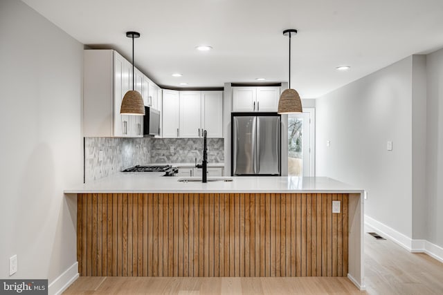 kitchen with sink, white cabinetry, kitchen peninsula, stainless steel appliances, and backsplash