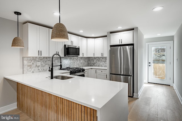 kitchen with pendant lighting, sink, appliances with stainless steel finishes, white cabinetry, and kitchen peninsula