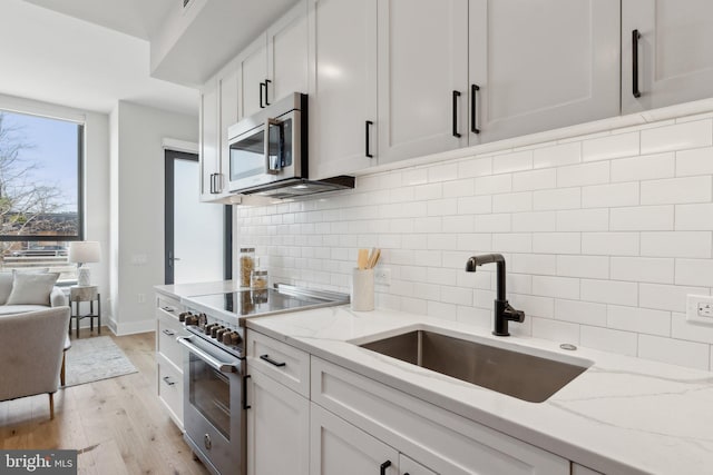 kitchen featuring sink, appliances with stainless steel finishes, white cabinetry, light stone countertops, and light hardwood / wood-style floors