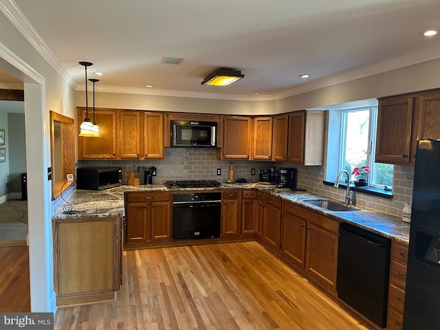 kitchen with brown cabinetry, stone counters, a sink, black appliances, and light wood-type flooring