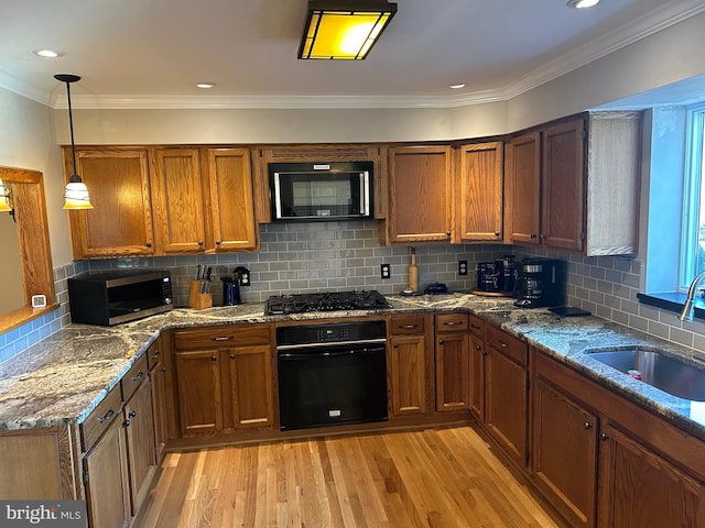 kitchen featuring brown cabinetry, black appliances, light wood-type flooring, and a sink