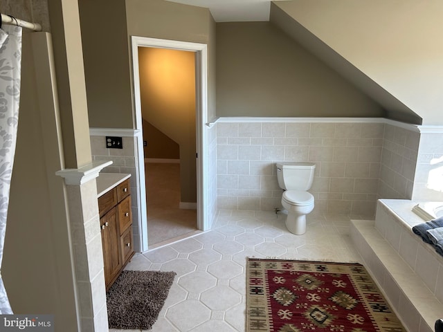 full bathroom featuring tile patterned floors, toilet, tile walls, and vaulted ceiling