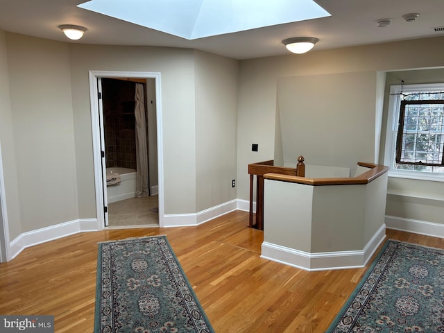 corridor with a skylight, an upstairs landing, baseboards, and light wood finished floors