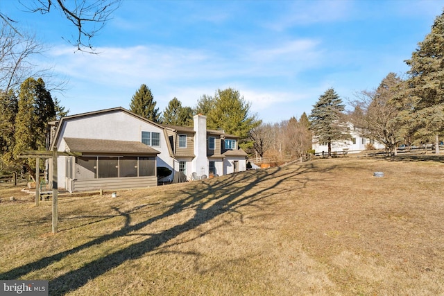 rear view of property featuring a chimney, a yard, and a sunroom