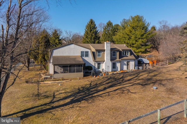 rear view of house with a gambrel roof, a sunroom, a chimney, and fence