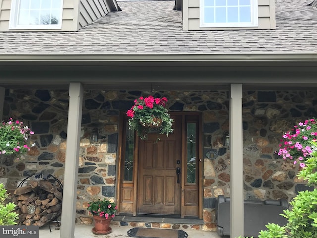 entrance to property featuring stone siding and roof with shingles