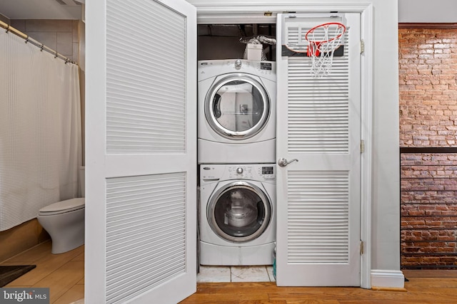 clothes washing area with stacked washer and dryer, brick wall, and light hardwood / wood-style flooring