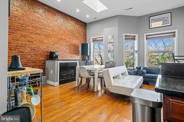 living room featuring light hardwood / wood-style flooring, a skylight, brick wall, and plenty of natural light