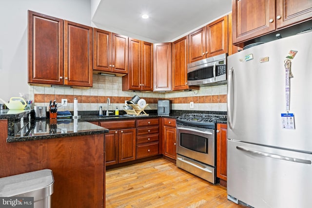 kitchen with sink, backsplash, dark stone counters, light hardwood / wood-style floors, and stainless steel appliances