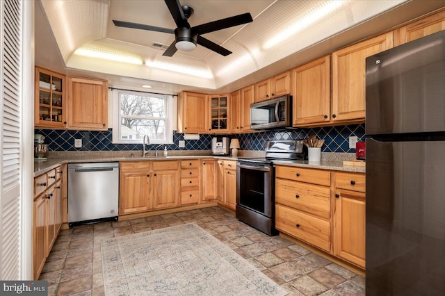 kitchen with stainless steel appliances, light stone countertops, a raised ceiling, backsplash, and sink