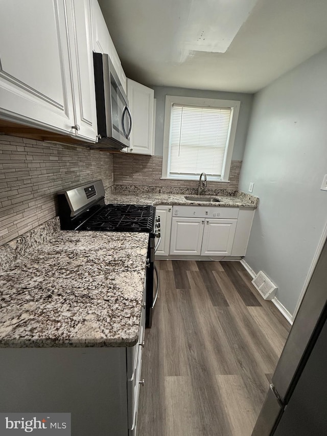 kitchen with dark wood-type flooring, sink, light stone counters, stainless steel appliances, and white cabinets