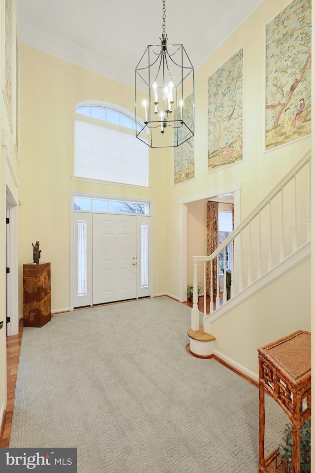 entryway with crown molding, carpet, a towering ceiling, and a notable chandelier