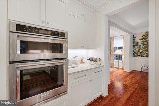 kitchen with light stone counters, double oven, ornamental molding, and white cabinets