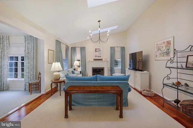 living room with hardwood / wood-style floors, a chandelier, and vaulted ceiling with skylight