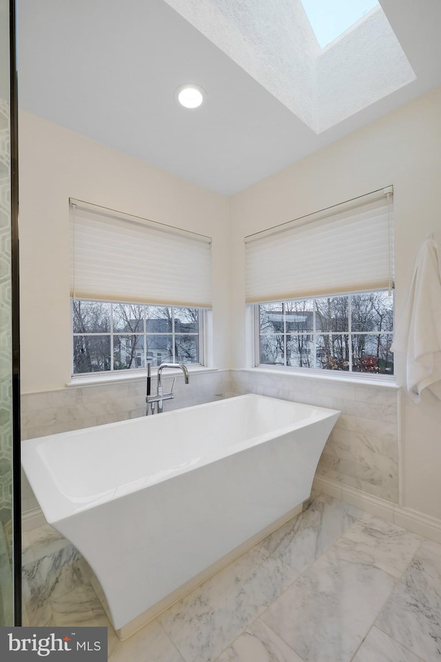 bathroom with a bathing tub, tile walls, and a skylight