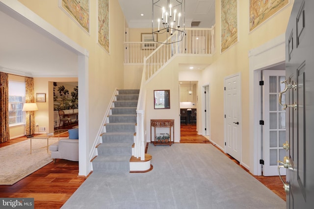 entryway featuring a high ceiling, ornamental molding, hardwood / wood-style floors, and a notable chandelier