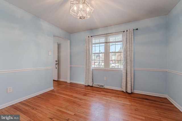 unfurnished room with a notable chandelier and light wood-type flooring