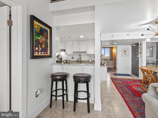 kitchen with sink, white cabinetry, light stone countertops, a kitchen bar, and kitchen peninsula