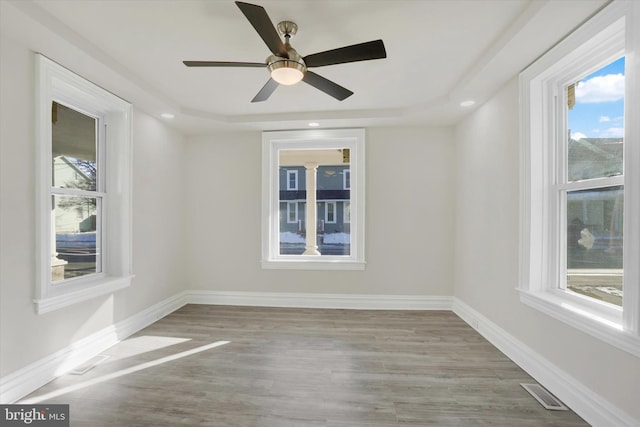 spare room with a tray ceiling, ceiling fan, and light wood-type flooring