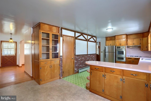 kitchen featuring sink, baseboard heating, stainless steel appliances, brick wall, and decorative light fixtures