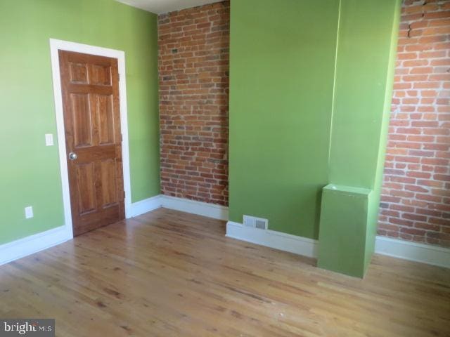 empty room with brick wall and light hardwood / wood-style flooring