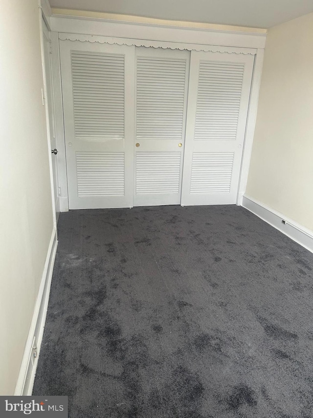 unfurnished bedroom with a closet and dark colored carpet