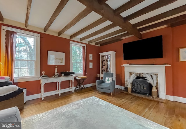 sitting room with beamed ceiling, a wood stove, and hardwood / wood-style floors