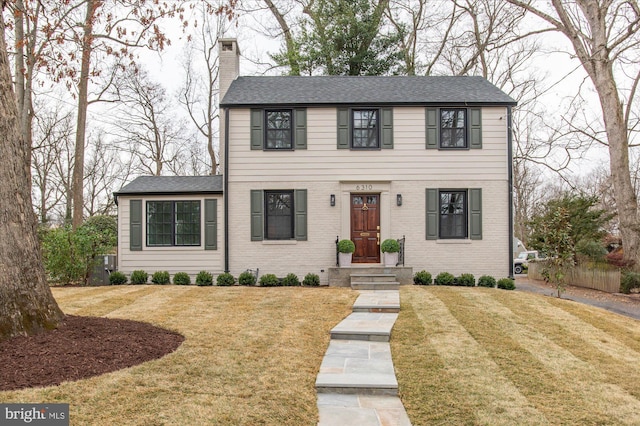 colonial-style house featuring brick siding, a chimney, and a front yard