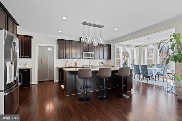 kitchen with dark wood-type flooring, tasteful backsplash, decorative light fixtures, appliances with stainless steel finishes, and a kitchen island with sink