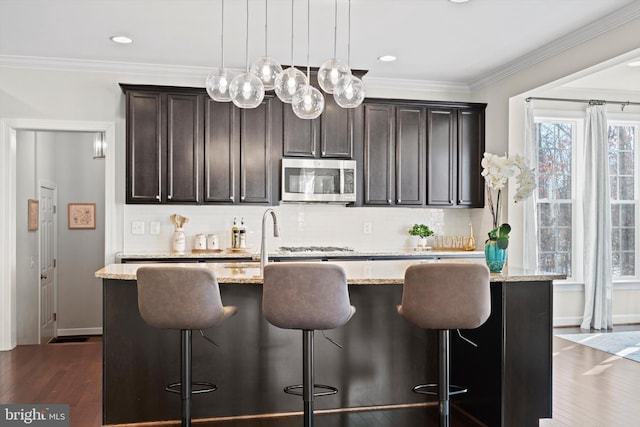 kitchen featuring a breakfast bar, light stone counters, decorative light fixtures, a kitchen island with sink, and backsplash