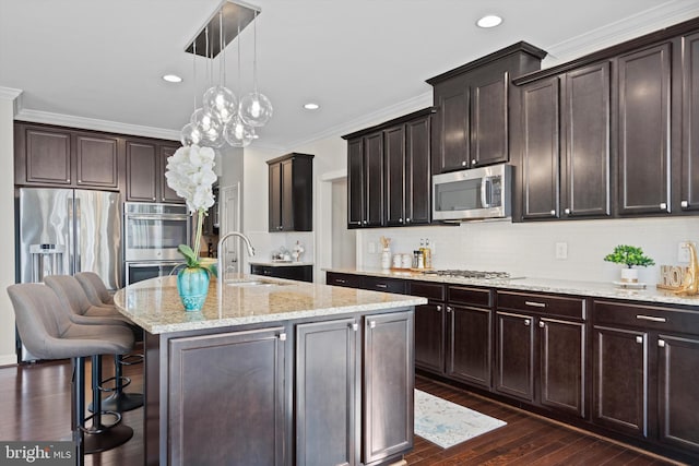 kitchen with decorative light fixtures, an island with sink, sink, dark brown cabinetry, and stainless steel appliances