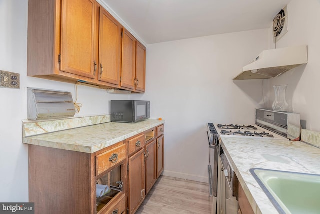 kitchen with sink, gas range oven, and light wood-type flooring