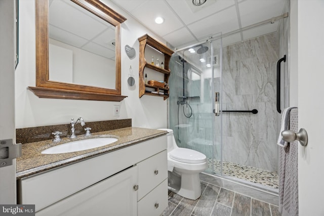 bathroom featuring a marble finish shower, wood finish floors, a drop ceiling, toilet, and vanity