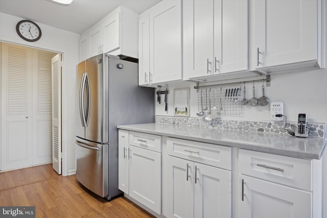 kitchen with white cabinetry, backsplash, light wood-type flooring, and freestanding refrigerator