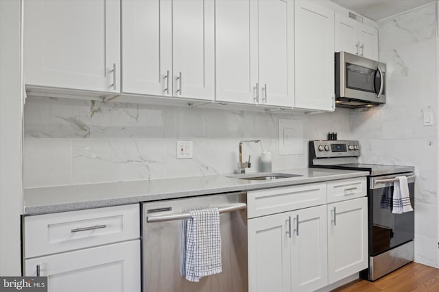 kitchen with tasteful backsplash, wood finished floors, white cabinets, stainless steel appliances, and a sink