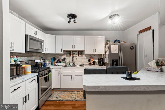 kitchen with appliances with stainless steel finishes, hardwood / wood-style floors, tasteful backsplash, sink, and white cabinets