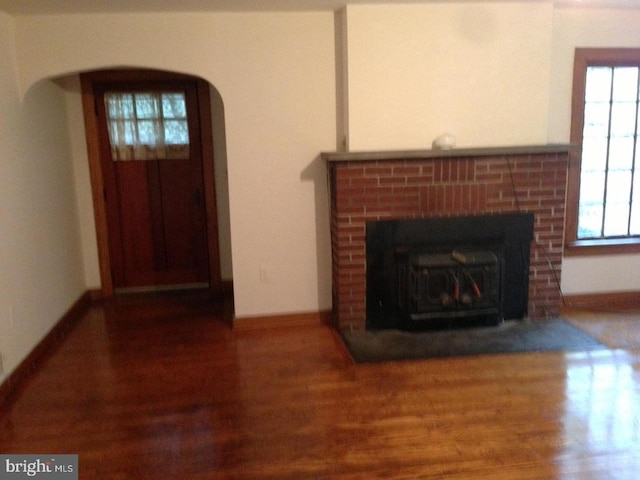 unfurnished living room featuring a brick fireplace and dark wood-type flooring