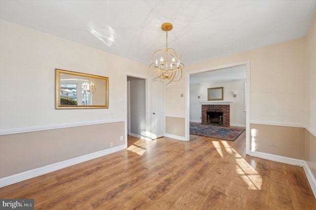 unfurnished living room with hardwood / wood-style floors, a brick fireplace, and a notable chandelier