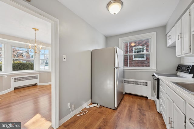 kitchen featuring range with electric cooktop, white cabinetry, stainless steel refrigerator, radiator heating unit, and pendant lighting